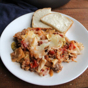 Plate of cabbage roll skillet meal topped with melted cheese and served with buttered bread.