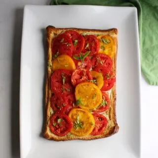 whole tomato tart on flaky puff pastry base with ricotta filling and fresh yellow and red tomatoes on top, ready to cut and serve.