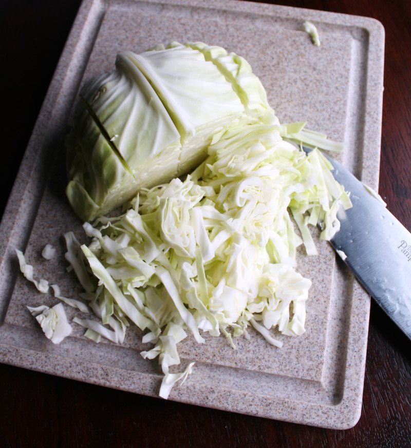 head of cabbage on cutting board being cut into small pieces for coleslaw.