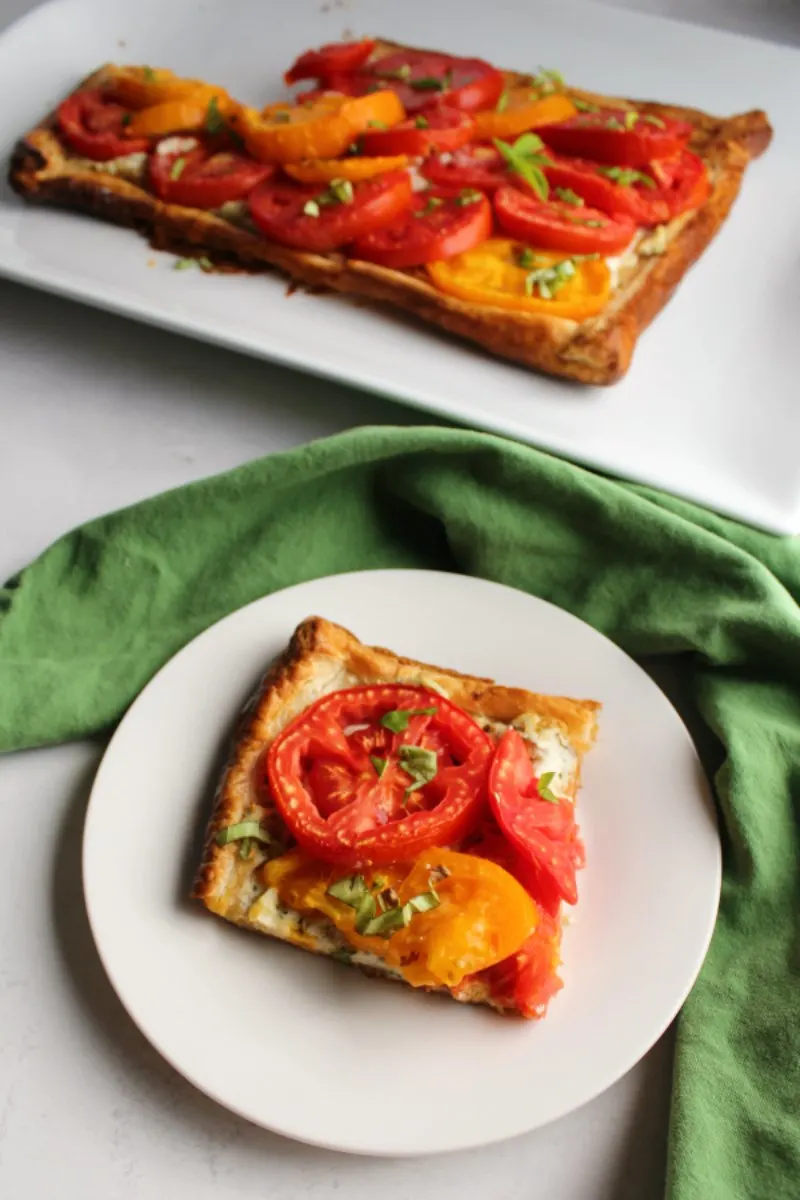 First slice of tomato tart served on plate with remaining tart in background.