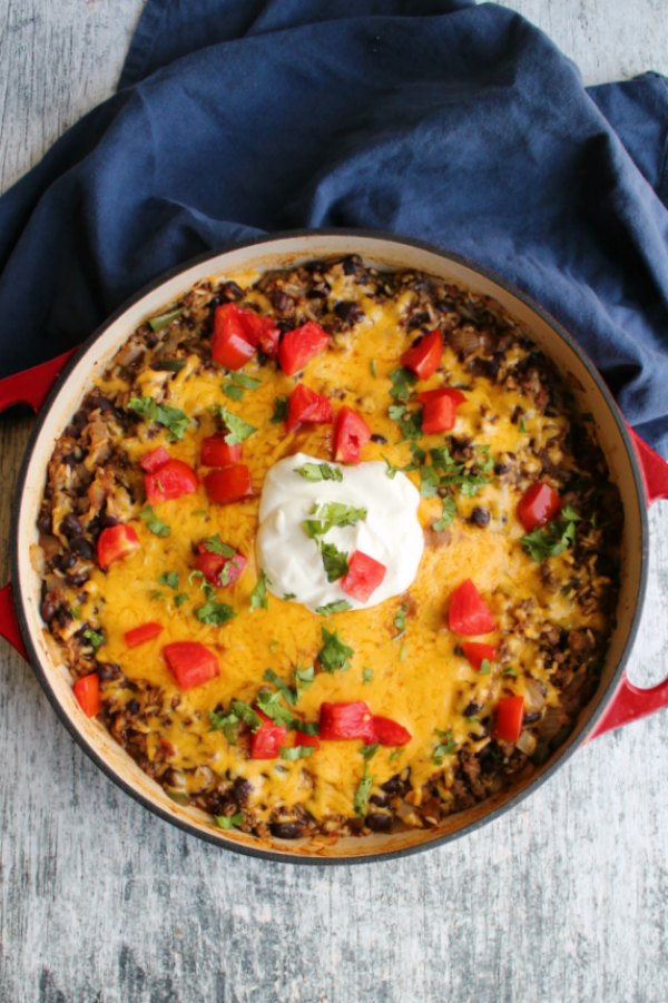 skillet full of one pan taco rice skillet meal topped with melted cheese, chopped tomatoes, cilantro and sour cream.