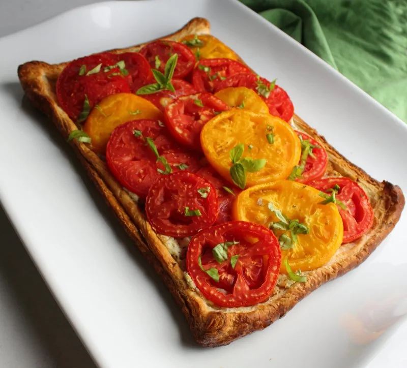 angled view of tomato tart with red and yellow tomato slices, fresh basil, ricotta and puff pastry.