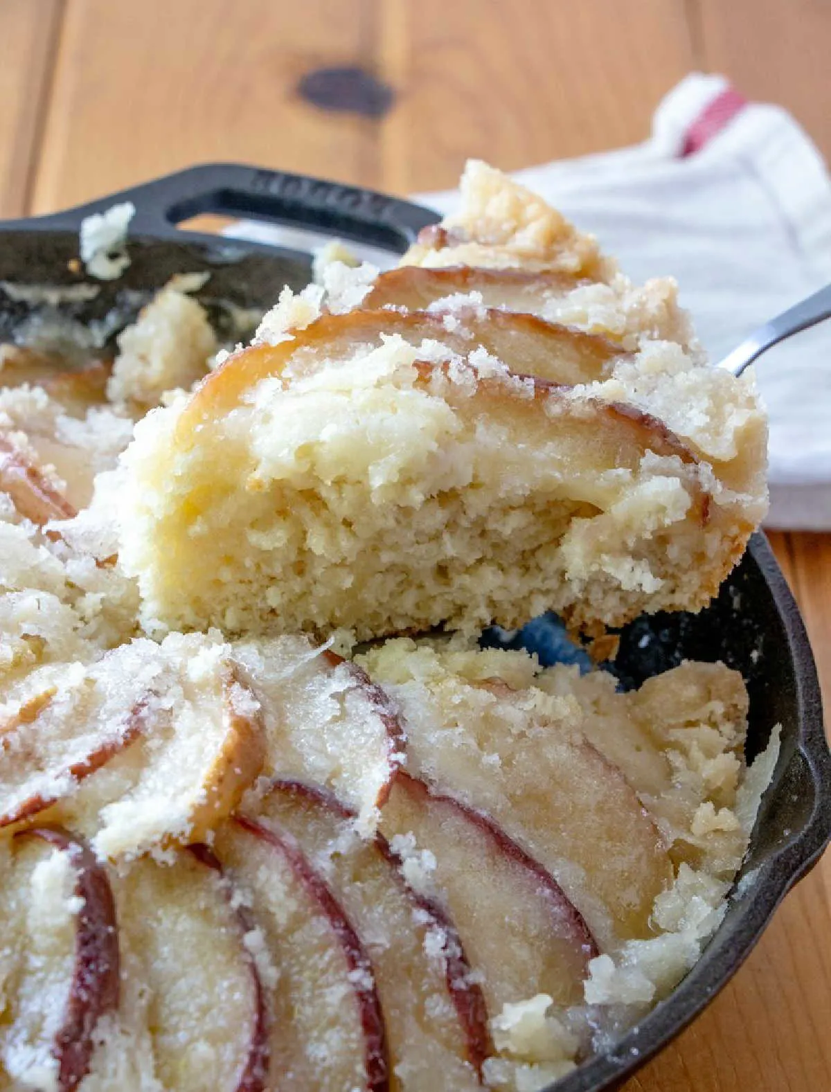 Lifting first slice of dutch apple coffee cake out of pan showing shortbread like texture of cake, fresh apple slices and buttery crumb topping.