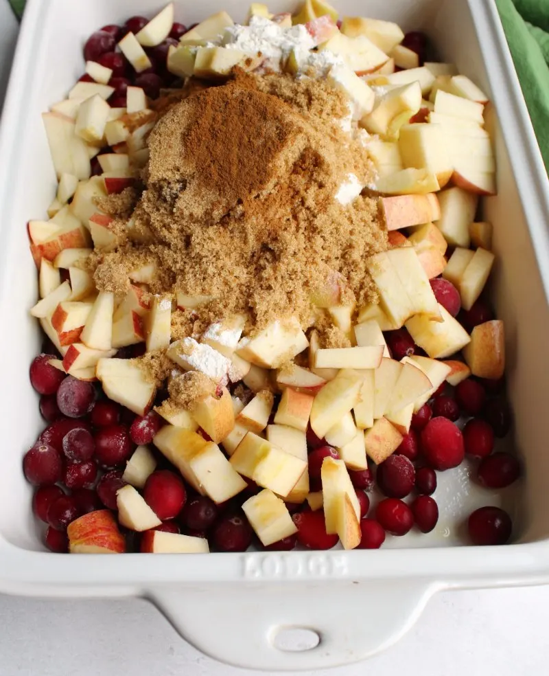 apple and cranberries in baking dish with brown sugar and cinnamon for making crisp.