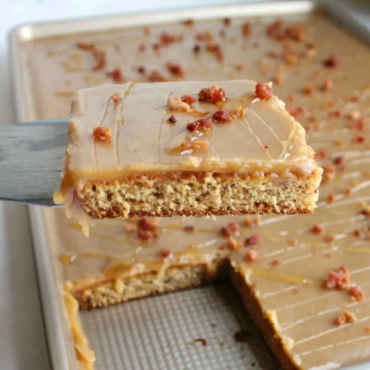 close shot of first slice of elvis sheet cake being lifted out of sheet pan showing moist banana cake, smooth peanut butter icing and crumbles of cooked bacon.