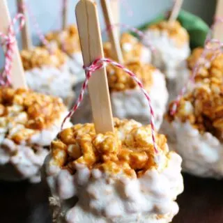 white chocolate dipped caramel apple popcorn balls with popsicle sticks and baking twine bows