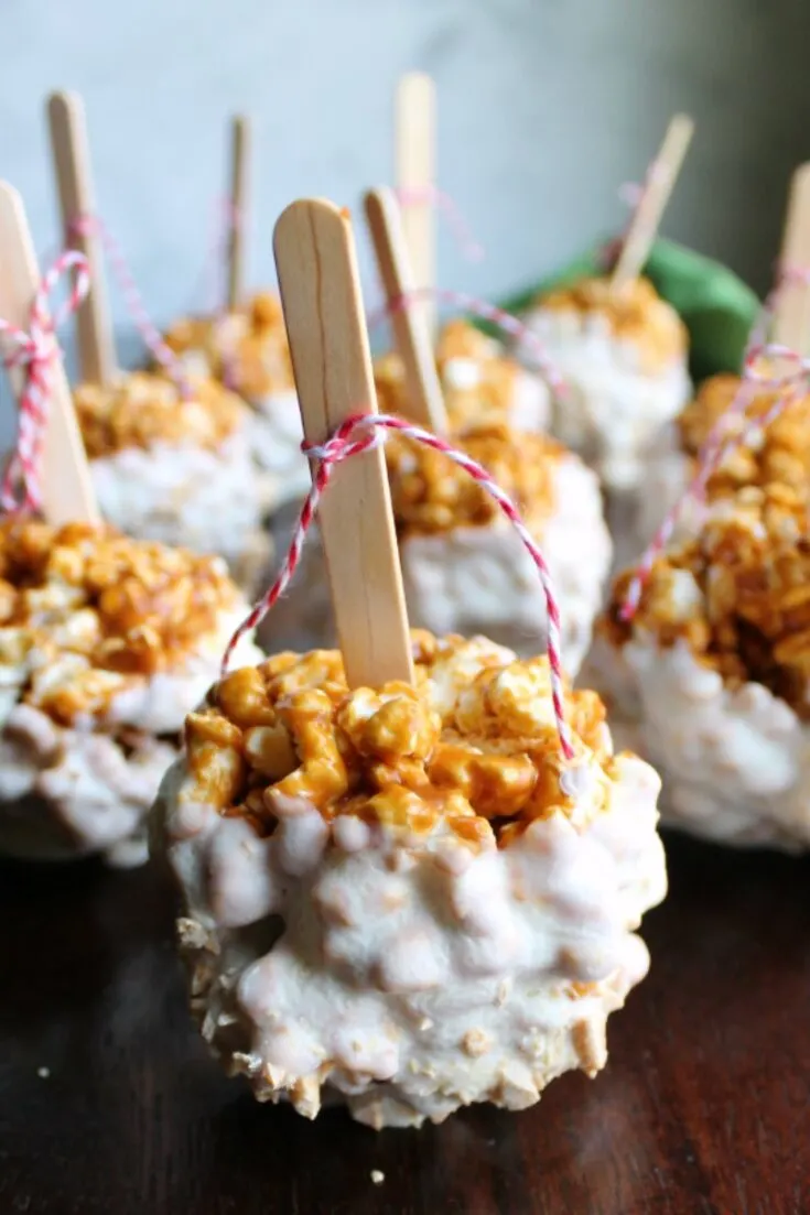 white chocolate dipped caramel apple popcorn balls with popsicle sticks and baking twine bows