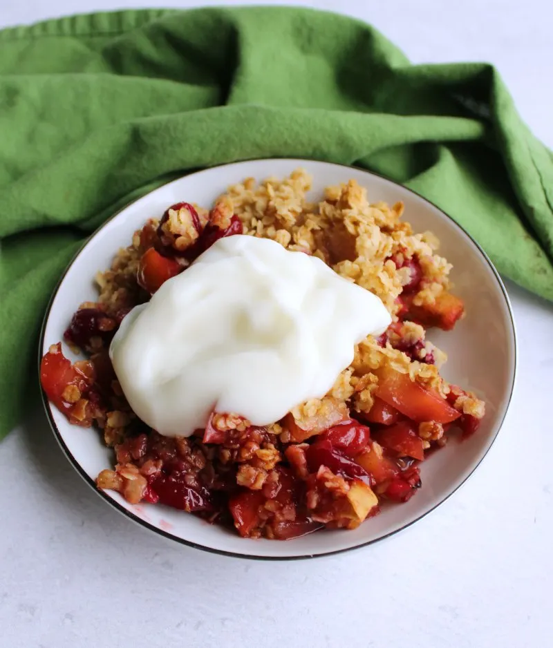 serving of cranberry apple crisp with dollop of yogurt on top.