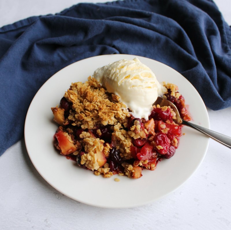 serving of cranberry apple crisp on plate with scoop of vanilla ice cream