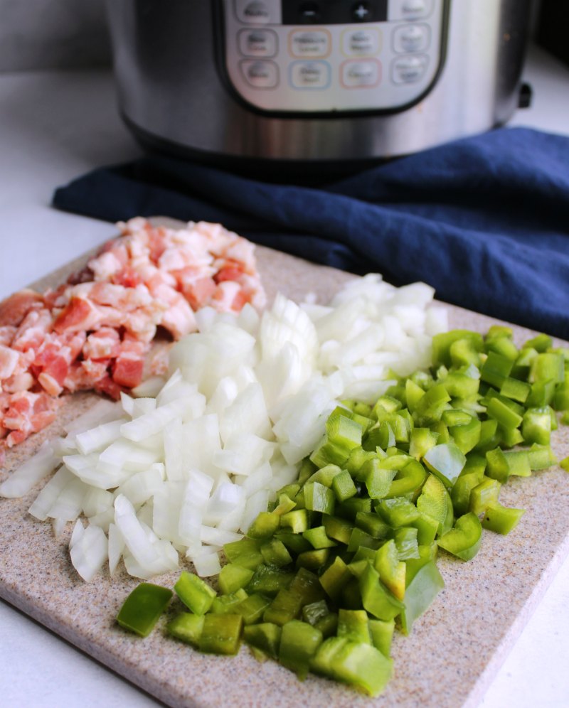 cutting board filled with chopped bacon, onions and green pepper in front of instant pot for maple baked beans.