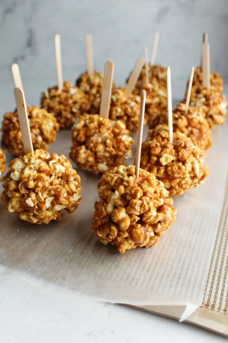 freshly formed caramel apple popcorn balls on wax paper with popsicle sticks inserted.