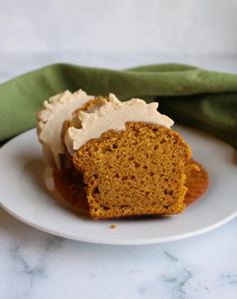 brown sugar frosting topped pumpkin cupcake cut in half with moist inside showing.