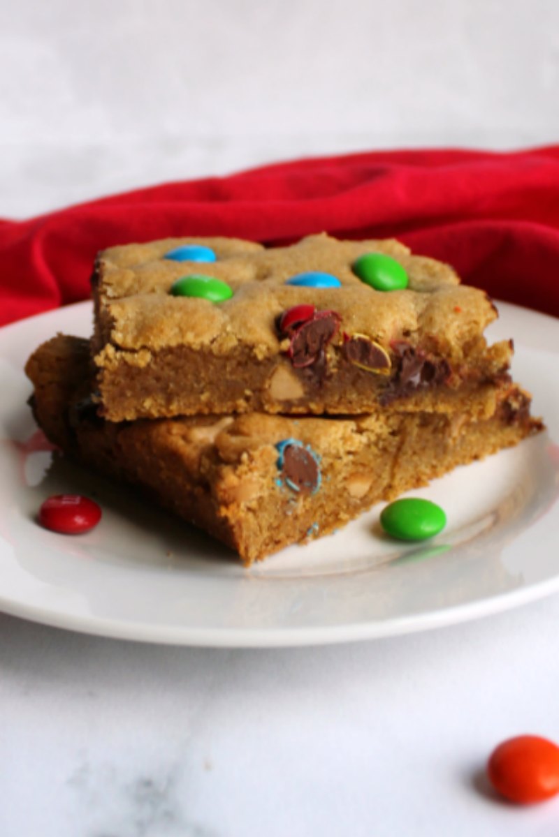 two pieces of chewy salted caramel m&m blondies stacked on plate with soft centers showing.