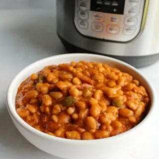 White serving bowl filled with maple bacon baked beans in front of instant pot.
