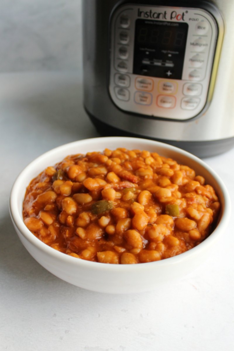 White serving bowl filled with maple bacon baked beans in front of instant pot.