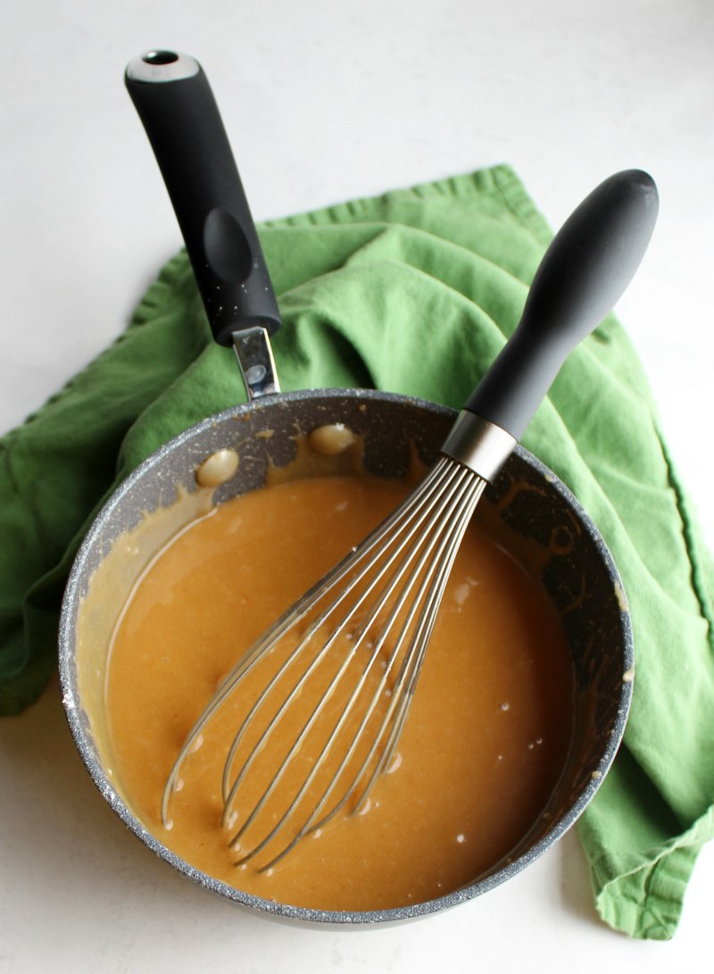 peanut butter icing in saucepan with whisk, ready for cake.