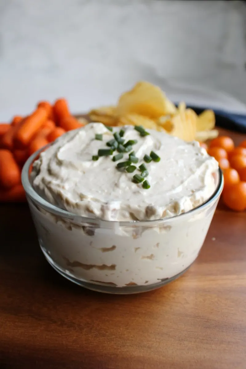 looking across a glass dish of creamy clam dip with vegetable and chip dippers in background.
