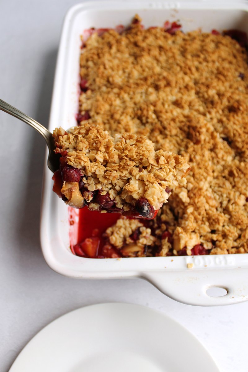 Serving spoon filled with cranberry apple crisp with golden oat topping being lifted out of the baking pan.