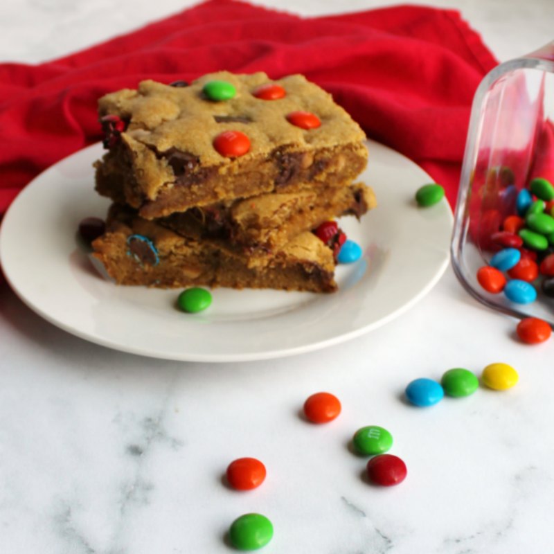 three pieces of chewy salted caramel m&m blondies stacked high on plate with candies scattered around.
