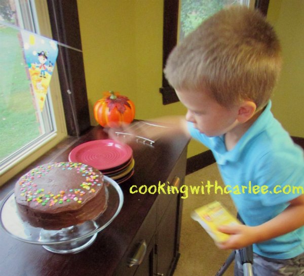 Small boy putting birthday candles in a layer cake with chocolate icing and sprinkles.