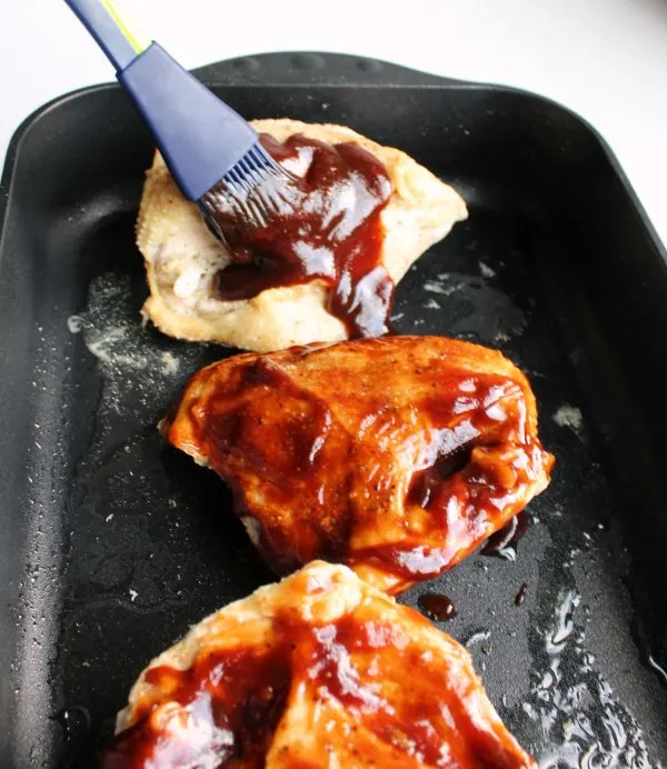 brushing bbq sauce on to baked chicken breast.