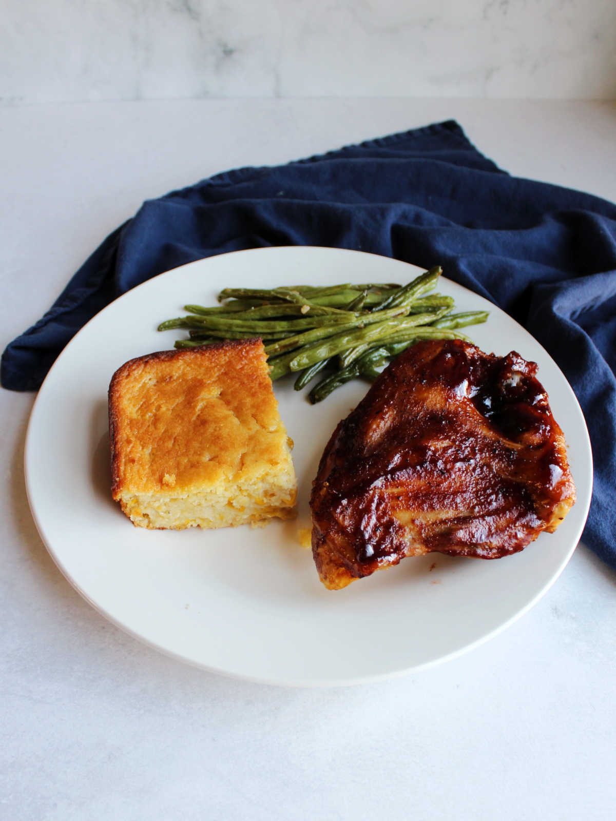 square piece of corn pudding on plate with bbq chicken and green beans ready to eat.