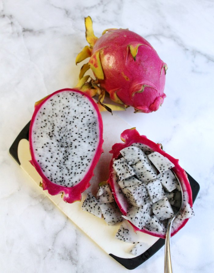 dragon fruit sliced in half with bright pink exterior and white interior speckled with seeds. Spoon scooping out chunks of fruit.