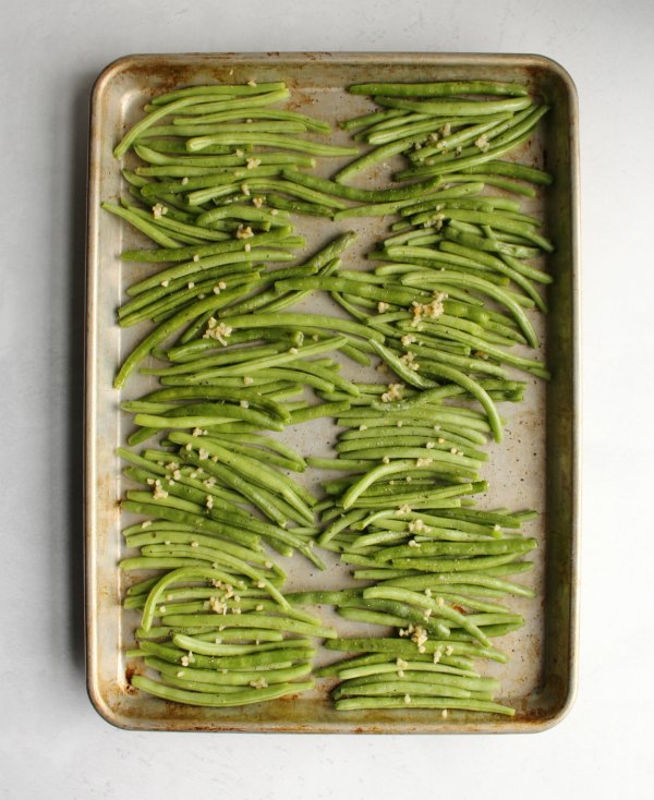 fresh green beans and chopped garlic on a sheet pan ready to be roasted