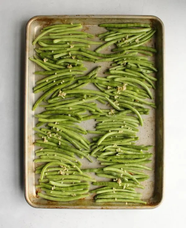 fresh green beans and chopped garlic on a sheet pan ready to be roasted