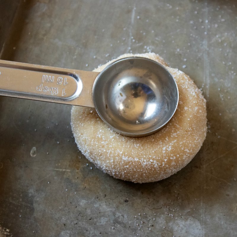 using a teaspoon to put an indent in a peanut butter thumbprint cookie.