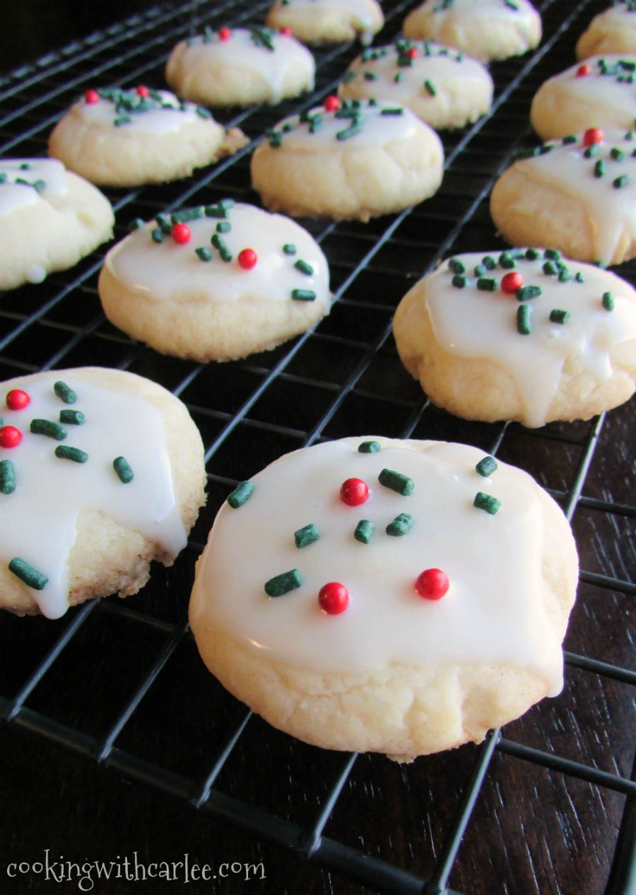 Tender melt in your mouth melting moments cookies with glaze and Christmas sprinkles on wire cooling rack.