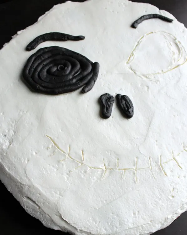 piping black frosting over traced lines on cupcake cake to start making the face details