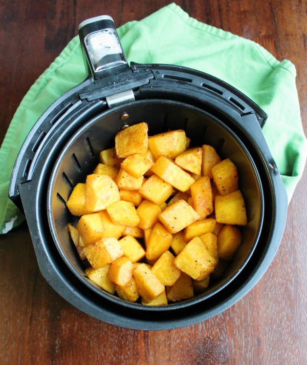 air fryer basket with roasted butternut squash cubes in it.
