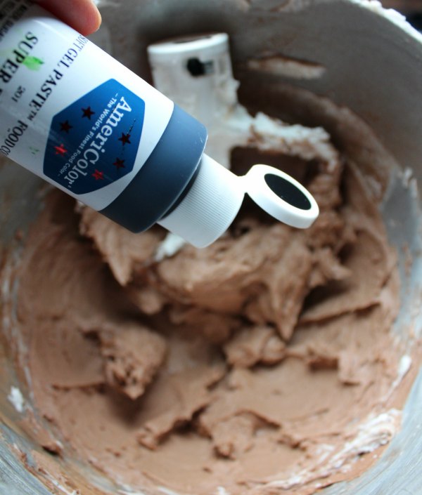 adding black food coloring gel to chocolate frosting to make black frosting