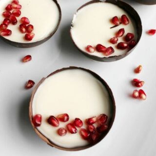 close up of dark chocolate bowls filled with vanilla yogurt panna cotta and topped with pomegranate arils.