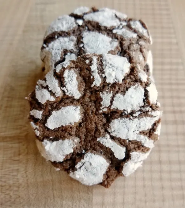 close up of the top of a powder sugar coated chocolate crinkle cookie leaned against a stack of cookies.