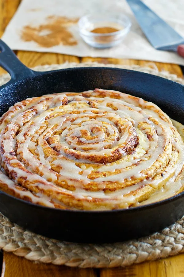 looking across the top of a fresh from the oven pumpkin spice skillet cinnamon roll with yummy maple brown butter glaze