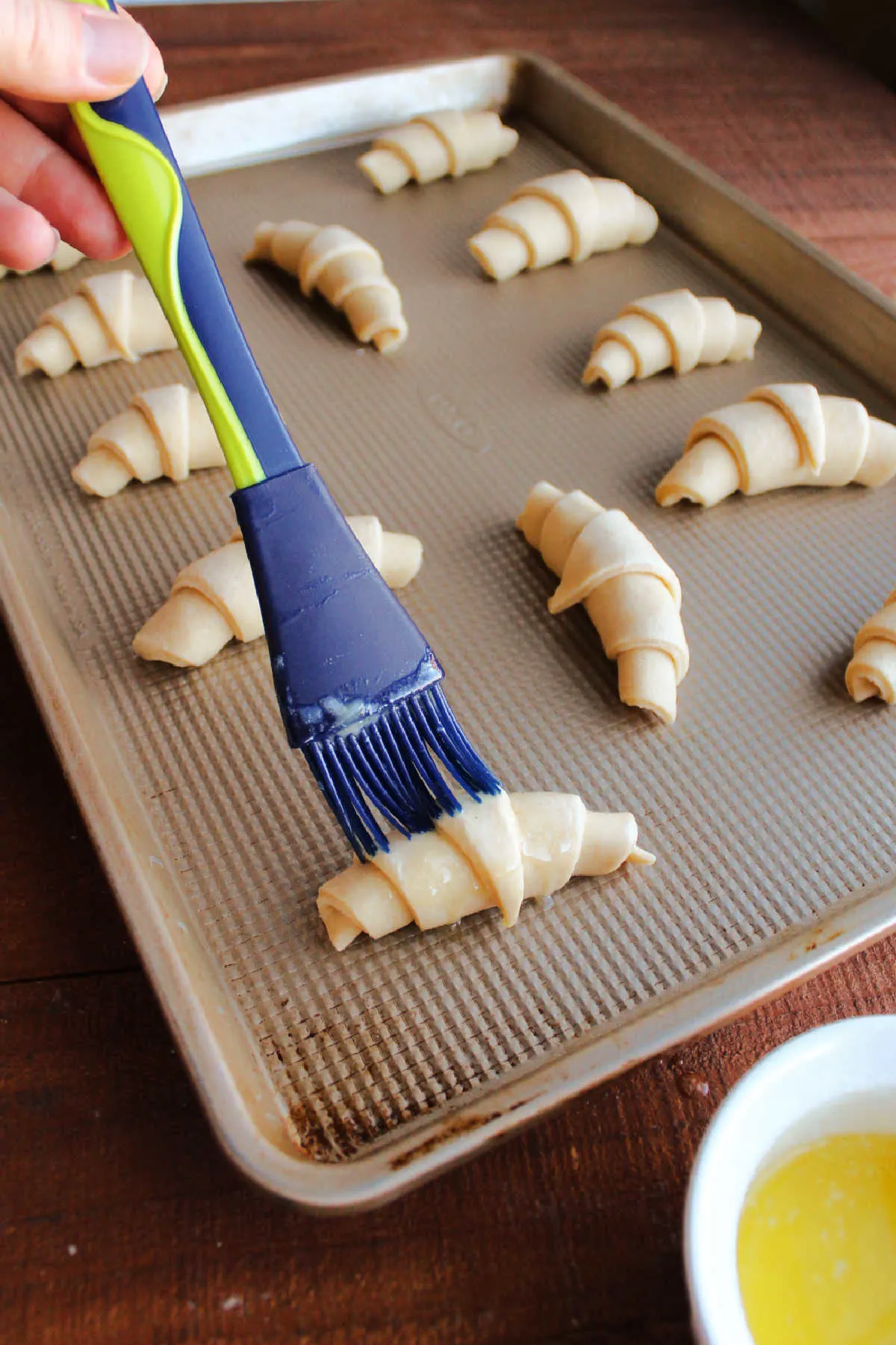 Brushing proofed crescent rolls with butter before they go into the oven.