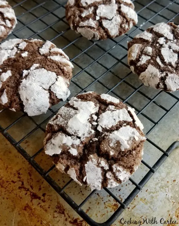 chocolate crinkle cookies with cracked powdered sugar surfaces cooling on wire rack.