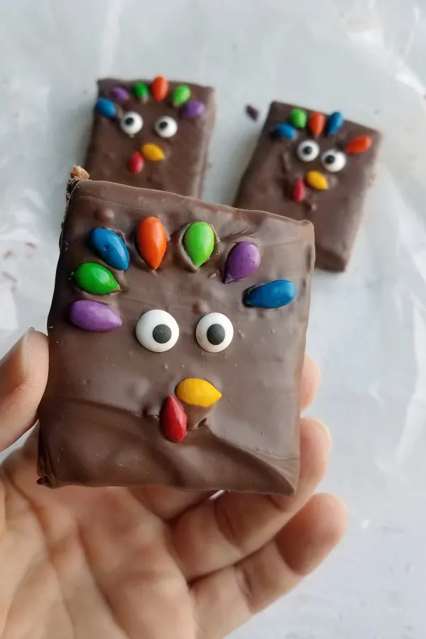 Hand holding Thanksgiving rice krispie treat decorated like a turkey with colorful sunflower seeds and candy eyes.
