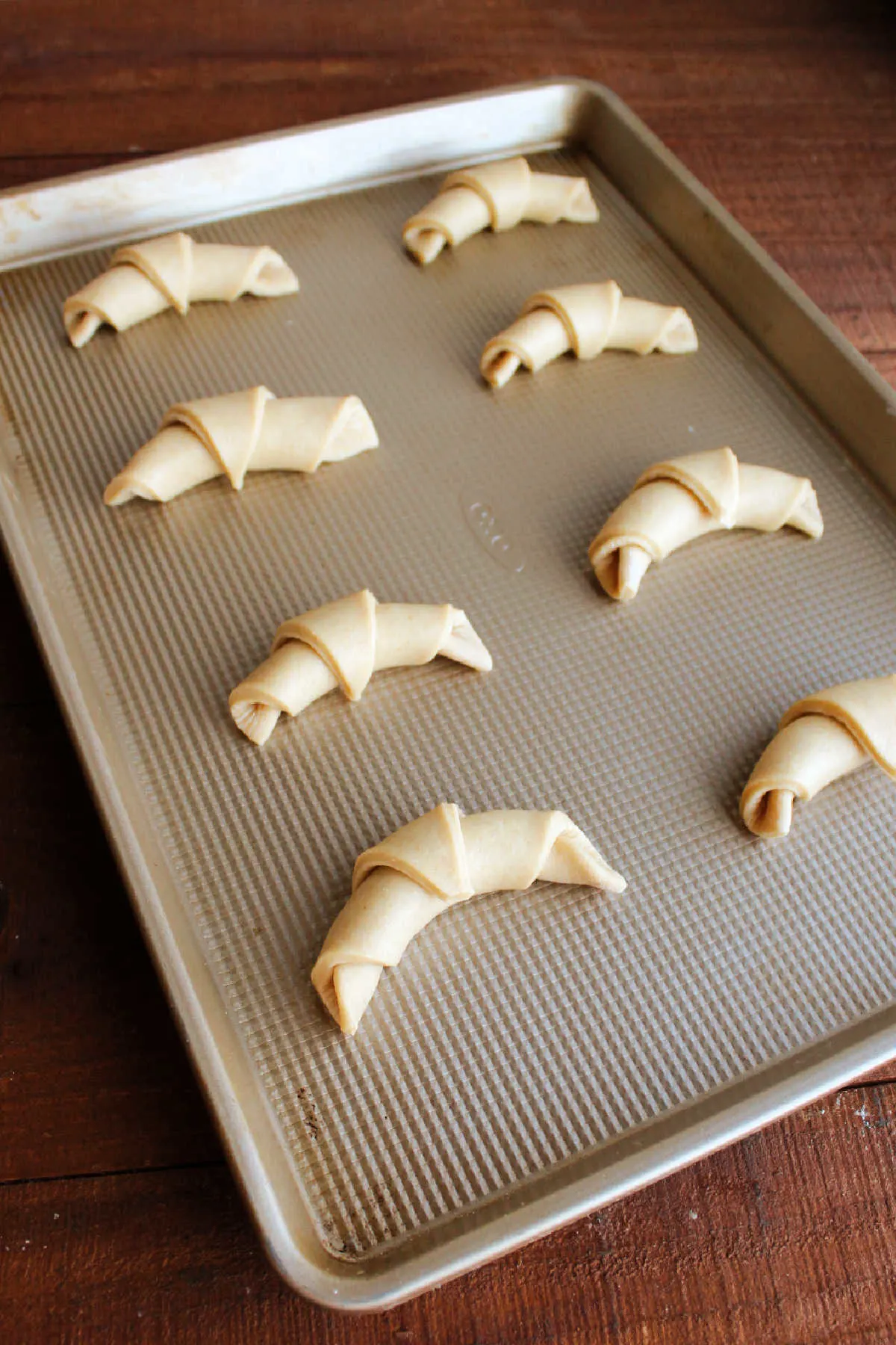 Baking sheet pan of crescent roll dough rolled into horns and ready to proof.