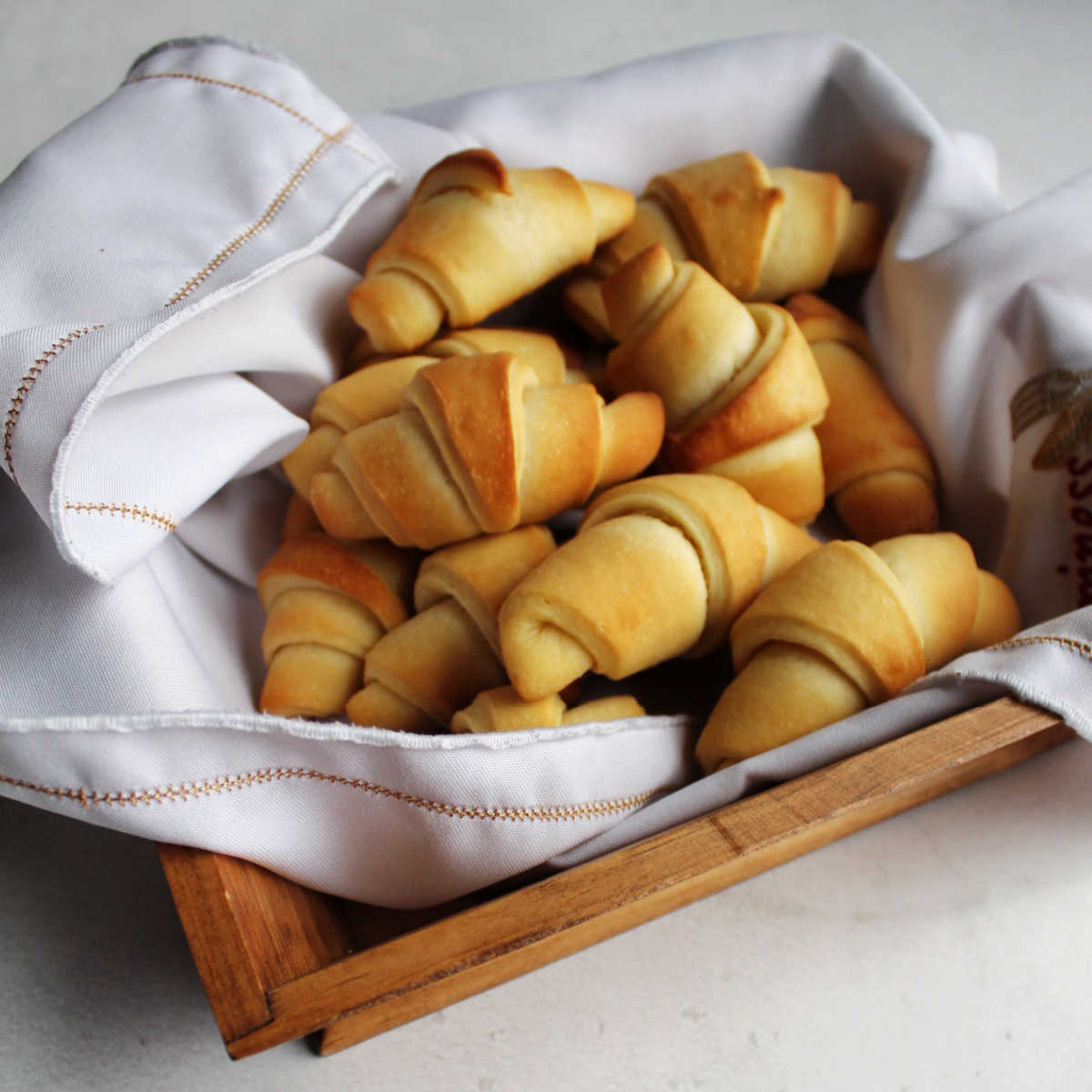 Basket of fresh homemade crescent rolls with buttery golden brown exterior and classic horn shape. 