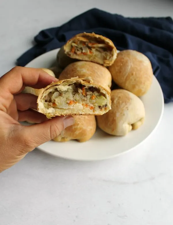hand holding half of a bierock (or runza) with mozzarella, cabbage and ground beef filling showing