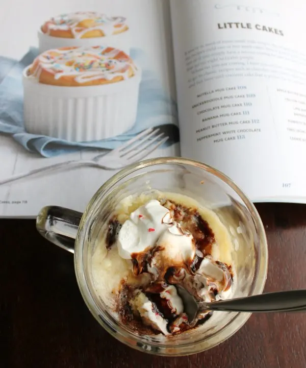 peppermint white chocolate mug cake with whipped cream and chocolate in front of easy cake cookbook.