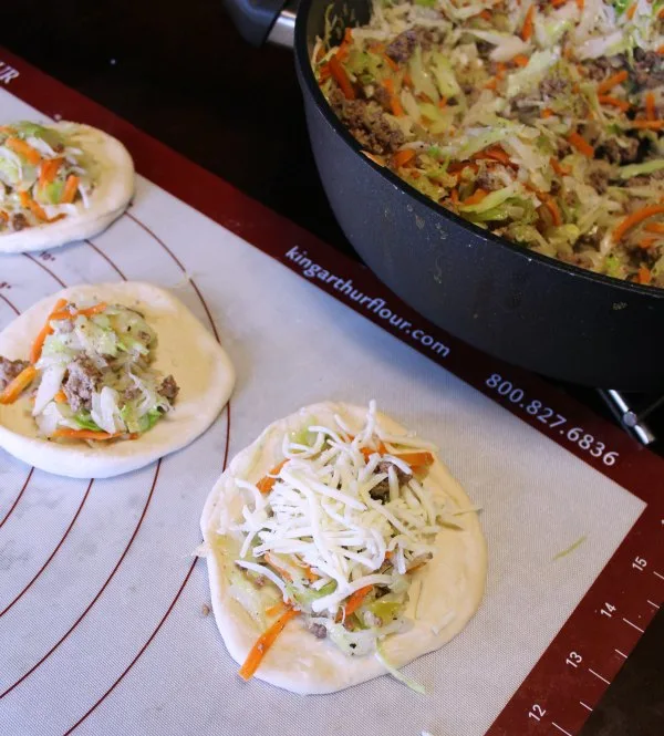 putting shredded cabbage and ground beef cabbage on flattened dough circles for runzas. 