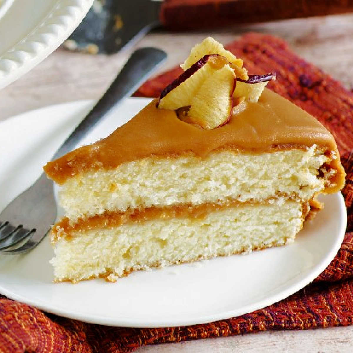 Slice of homemade buttery vanilla cake with homemade caramel frosting topped with apple chips.