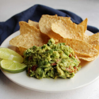 close up of plate with tortilla chips, chunky guacamole and slices of lime.