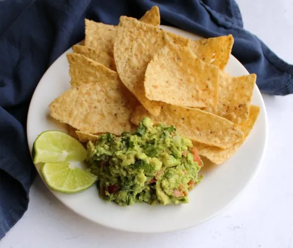 serving of homemade guacamole with chips and lime wedges.