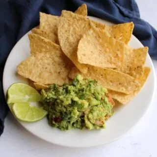 close up of plate with tortilla chips, chunky guacamole and slices of lime.