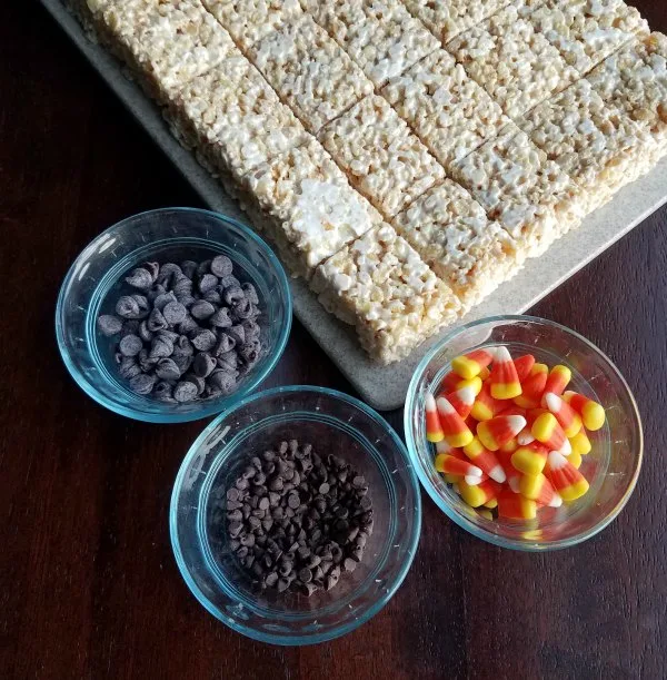 white rice krispie treats with bowls of mini chocolate chips, chocolate chips and candy corn.
